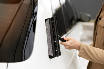 Obraz premium Closeup man washing his car at self-service car wash using window scraper, professional worker
