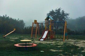 Rural playground, equipped with slides, various swings and ladders, early morning, autumn, light fog enveloped everything around, a mysterious atmosphere in an empty area