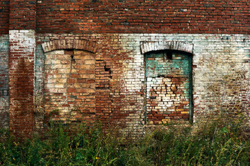 Wall of an old abandoned factory, old brick, painted in places, arched windows tightly bricked up,...