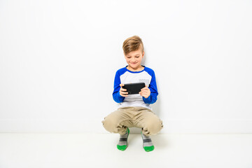 Cute little boy playing game over smartphone on white studio background.
