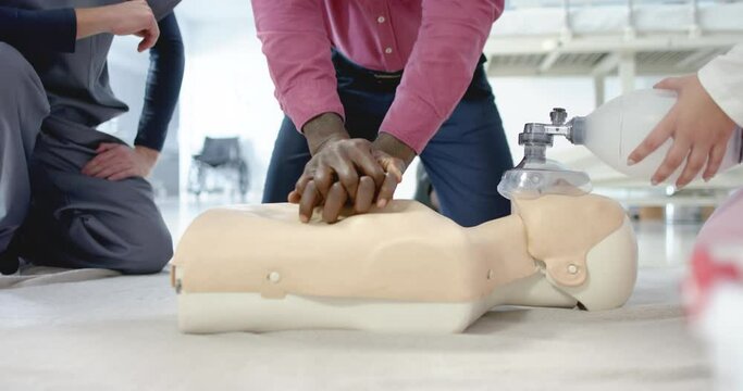 African american doctor training trainee doctors in emergency cpr procedure using dummy, slow motion