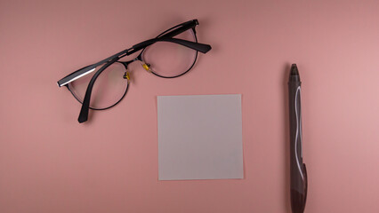 eyeglasses, a white sheet and a black pen lie on a pink background