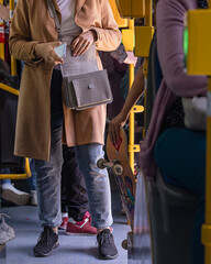 Multicultural passengers of different ages at rush hour ride inside public transport, standing with different items in a modern bus, public electric transport in Poland. Passenger with smartphone