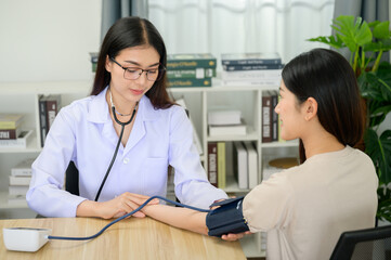 Portrait of Asian female doctor measuring heart and blood pressure while taking care of beautiful asian patient in medical consultation - obrazy, fototapety, plakaty