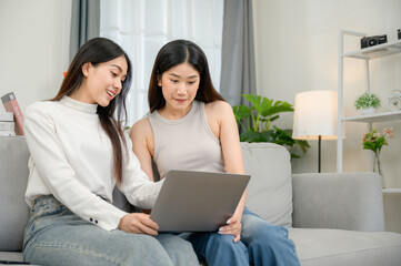 Two happy young women looking at laptops sitting on the sofa in the living room at home. and work online with a laptop computer Friends are excited about online shopping.