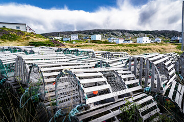 Wooden traditional lobster traps stacked on a shoreline overlooking small rustic homes along the East coast of Canada in Keels Newfoundland and Labrador.