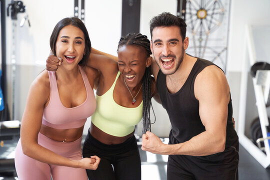 group of fitness friends flexing their arm very happy and smiling at the gym