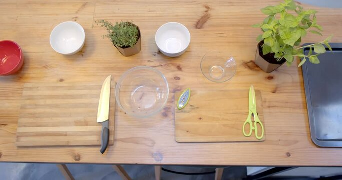 Overhead view of bowls, cutting boards and knife on wooden table in kitchen, slow motion