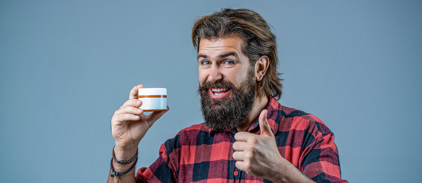 Bearded man with cream in his hands shows a thumbs up. Cream conditioner for men. Expert care for demanding hair. Plastic container with cream. Man holds bottle of cream or shower gel