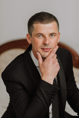 portrait of a young man in a white shirt and tie holding his chin with his hand. The groom is preparing for the wedding ceremony.