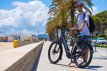 Male Cyclist in casual clothing, protective helmet and mirrored glasses riding on a bike near the...