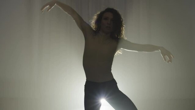 Silhouette of a woman performing an expressive dance in a beam of white light. An active and sensual manifestation of oneself in a dance on high heels. High quality 4k footage