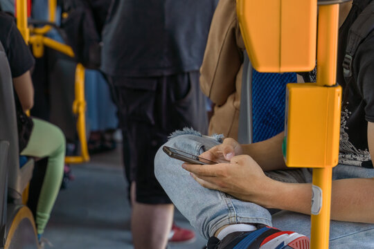 Smartphone in the hands of a teenager in the bus. Authentic multicultural passengers of different ages during rush hour ride inside public transport, public electric transport in Krakow, Poland - Powered by Adobe