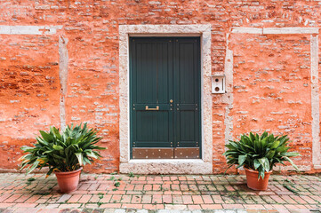 Red brick facade of the house with wooden door in Venice, Italy.