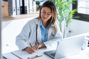 Serious female doctor working with her laptop in the medical consultation.