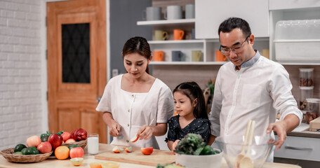 The family members happily and playfully prepare a bowl of various types of fruity and vegetable salad. Making quirky faces, joking, laughing, smiling, can create a good mood and positive atmosphere.