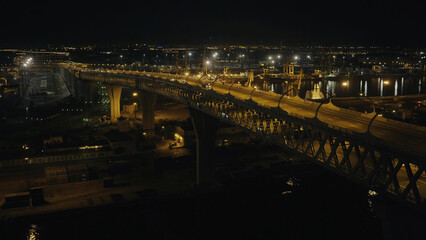 Car moving on multilevel night highway along construction site in sea port