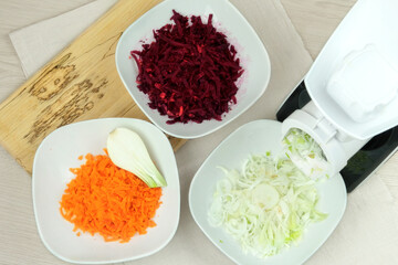 Carrots, beets and onions in a vegetable cutter on kitchen table. Chopped vegetable is falling into a bowls. Homemade healthy food.
