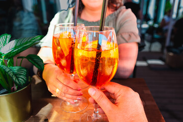 Couple celebratory toast with aperol spritz orange alcoholic cocktails at outdoors cocktail bar at night.Close up.