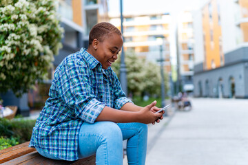 portrait of a young a student sitting on a bench and using her phone to talk to her friends