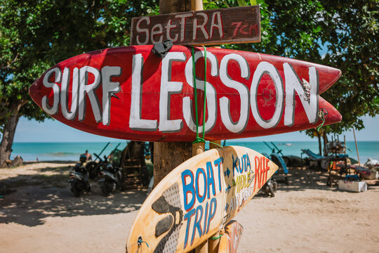 A red surfboard as a signpost with the inscription Surf lesson on Kuta beach in Bali.