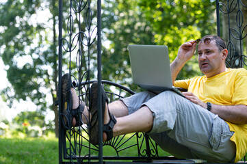 senior man with laptop working outside in garden, green home office concept.