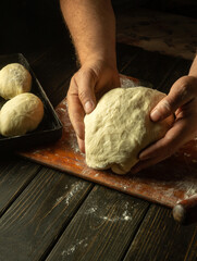 Male hands prepare dough for buns on the table close-up. Baker baking pies at home.