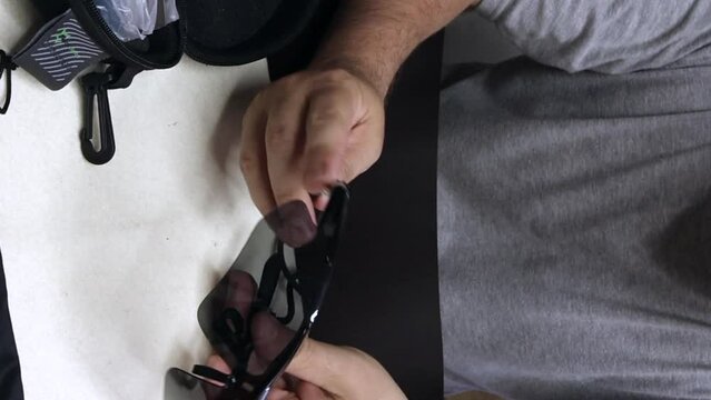 A man is holding sunglasses with a drawstring on the temples. Glasses with interchangeable colored lenses. A blogger makes a review of sunglasses. Vertical video.
