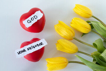Love God and your neighbor, handwritten text, red hearts, and yellow tulips on white. Top view....