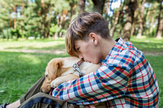 Teenage boy hugs labrador dog in park in summer. Friendship and pets concept.