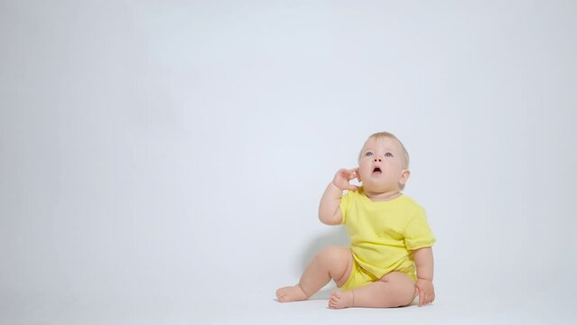 a baby sitting on his ass yawns, slaps his ear, showing gestures of indifference