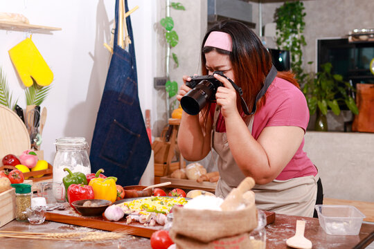 Fat girl cooking in the kitchen holding a camera to take pictures of food placed on the table. Food concept. Chef cooking
