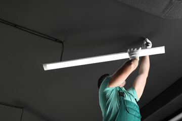 Ceiling light. Electrician installing led linear lamp indoors. Space for text - obrazy, fototapety, plakaty