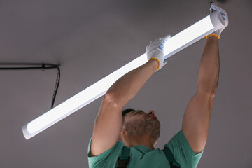 Ceiling light. Electrician installing led linear lamp indoors, low angle view