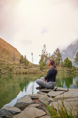 vertical photo of latin woman on vacation meditating on the shores of a lake with mountains in bolivia