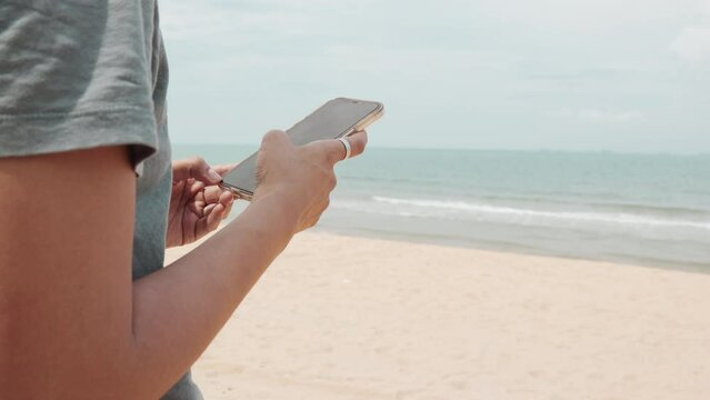 Asian woman on her enjoyable journey of freedom and outdoor enjoyment on the beach abd sea. With smartphone in hand, she captures moments of happiness, sharing them in the digital social network.