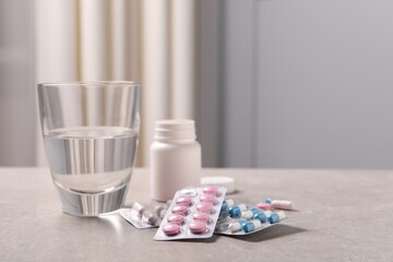 Different pills in blisters, medical bottle and glass of water on grey table. Space for text