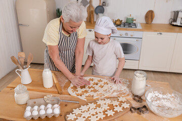 Happy family in kitchen. Grandmother granddaughter child cutting cookies of dough on kitchen table together. Grandma teaching kid girl cook bake cookies. Household teamwork helping family generations