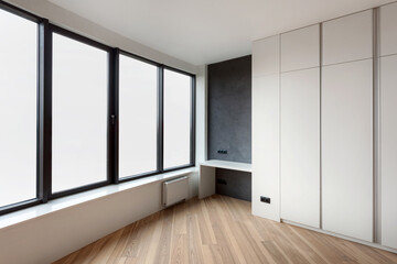 wardrobe with white facade, home office table and large windows in room