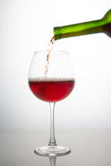 red wine from a bottle is poured into a glass on a light background. alcoholism and addiction. drinks for the holiday