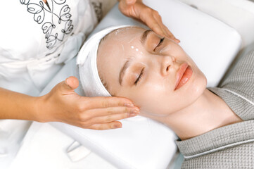 Facial skin care. Caucasian relaxed woman with eyes closed makes procedures in the salon, receives...