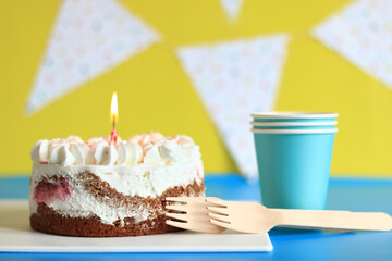 Festive cake with a birthday candle. Cake, paper cups and forks. Cake on a festive background with birthday flags. Happy birthday