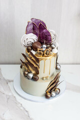 Elegant tall two-layered grey and golden cake for a man's anniversary, decorated with isomalt, meringues, chocolate spheres and petals
