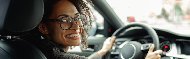 Smiling woman manager driving car and holding both hands on steering wheel on the way to work