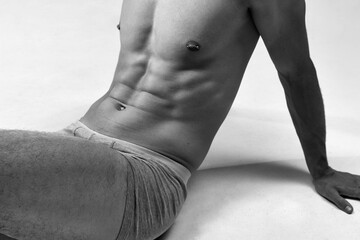 Black and white cropped image of male muscular, relief, fit, strong body. Model posing on floor in underwear. Concept of male natural beauty, body care, health, sport, fashion, ad, art