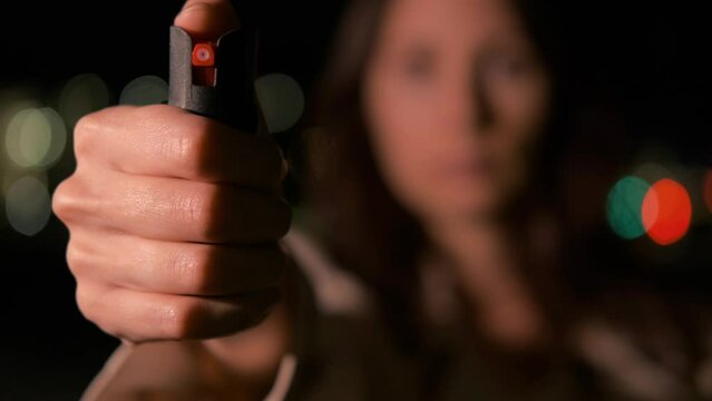 An unrecognizable figure of a woman in the dark close-up points a pepper spray with her hand directly at the camera, blur