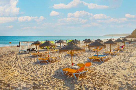 Rows Of Deck Chairs And Umbrellas On Sandy Beach Along Algarve In Portugal