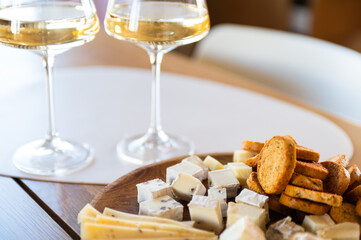 different types of cheese, with mold, hard, with spices, etc. lies on wooden plate on a wooden table and glass of white wine. a delicious and healthy snack for wine.  Selective focus