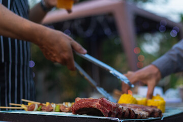 Meat and skewers ingredients for barbecue party are placed on grill to cook barbecue and make it ready for family to join barbecue party tonight.  party background image has Copy Space for text.