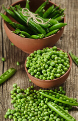 Fresh green peas in pods and peeled green peas in bowls, scattered pea grains on a wooden background.